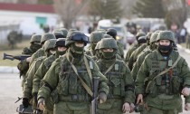 Military personnel, believed to be Russian servicemen, walk outside the territory of a Ukrainian military unit in the village of Perevalnoye outside Simferopol